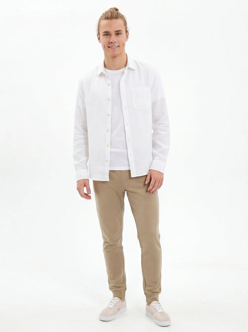 Man wearing a white shirt and beige pants on a white background