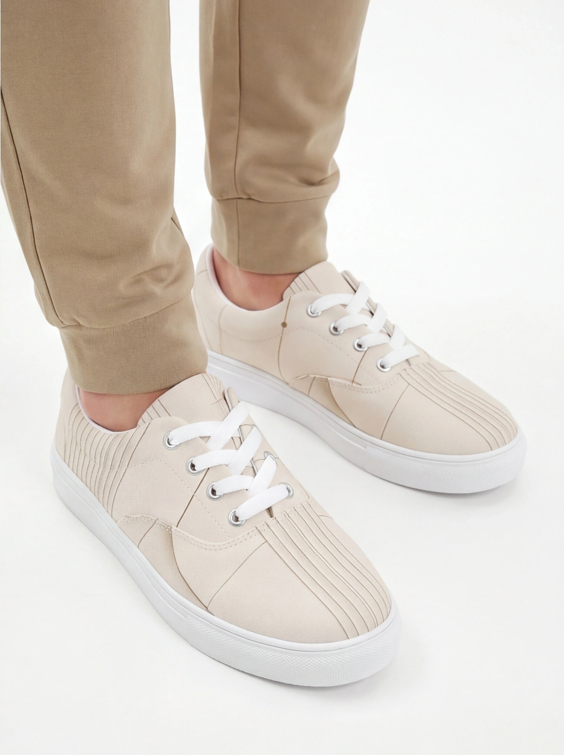 Beige sneakers with white laces worn with beige pants on a white background
